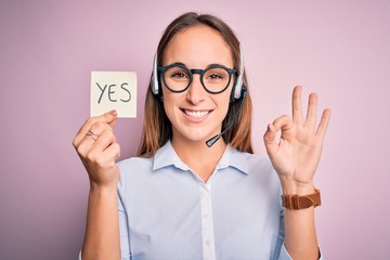 Beautiful call center agent woman working using headset holding reminder with yes message doing ok...
