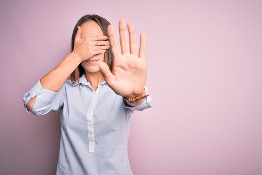 Young beautiful businesswoman wearing elegant shirt standing over isolated pink background covering eyes with hands and doing stop gesture with sad and fear expression. Embarrassed and negative