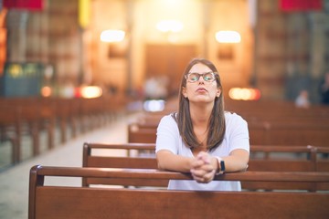 Young beautiful woman praying on her knees in a bench at church