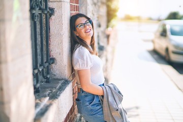 Young beautiful woman smiling happy and confident. Standing with smile on face leaning on the wall at the town street