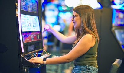 Young beautiful woman smiling happy and confident. Sitting with smile on face playing slot machine...