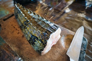 Complete crocodile tail being freshly prepared on a wooden board for cooking
