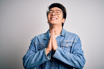 Young handsome chinese man wearing denim jacket and glasses over white background begging and...