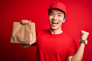 Young handsome chinese delivery man holding takeaway paper bag with food screaming proud and celebrating victory and success very excited, cheering emotion
