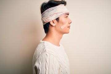 Young handsome chinese man injured for accident wearing bandage and strips on head looking to side, relax profile pose with natural face and confident smile.