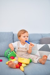 Adorable blonde toddler sitting on the sofa playing with plastic meals toys at home