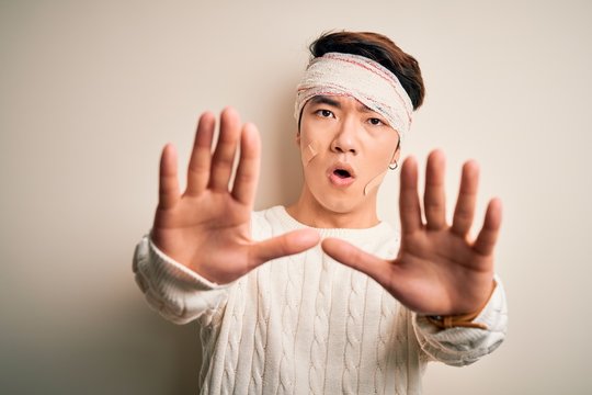 Young handsome chinese man injured for accident wearing bandage and strips on head doing stop gesture with hands palms, angry and frustration expression
