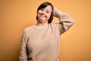Young down syndrome woman wearing casual sweater over yellow background confuse and wonder about question. Uncertain with doubt, thinking with hand on head. Pensive concept.