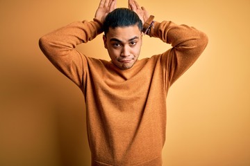 Young brazilian man wearing casual sweater standing over isolated yellow background Doing bunny ears gesture with hands palms looking cynical and skeptical. Easter rabbit concept.