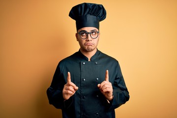 Young brazilian chef man wearing cooker uniform and hat over isolated yellow background Pointing up...