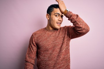 Young brazilian man wearing casual sweater standing over isolated pink background surprised with hand on head for mistake, remember error. Forgot, bad memory concept.