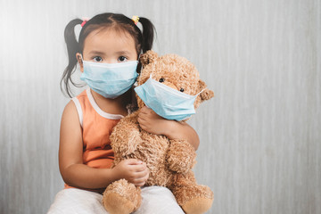 Little asian girl child holding a teddy bear wearing a mask. Concept of pediatric health care and infection