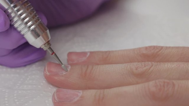 Young woman removes gel shellac polish from nails using manicure machine, close up shot