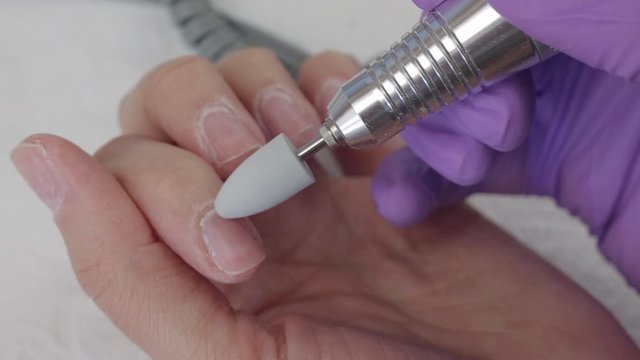 Young woman removes gel shellac polish from nails using manicure machine, close up shot