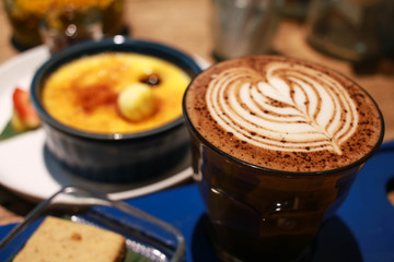 Cafe latte with latte art on a cup with Vanilla Crème Brûlée on the background.