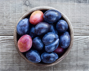 Plum in a wooden bowl on a wooden table. Fresh plum harvest from the garden. Top view