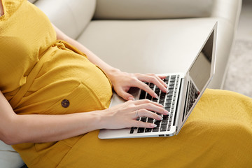 Fototapeta premium Cropped image of pregnant woman with laptop answering e-mails when working from home during quarantine