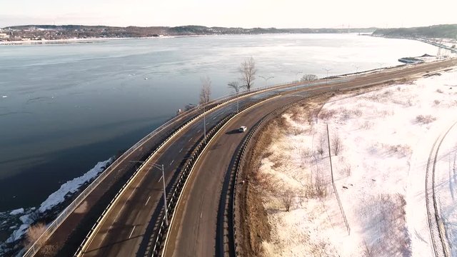 A small car passes on a highway near a large river. Filmed during winter in Quebec City, Canada.