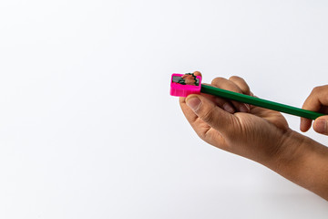 Young children hand using pink color pencil sharpener for pencil shaving his color pencil on white...