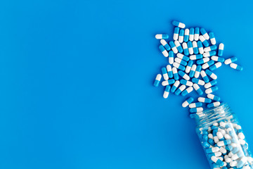 Blue and white capsules poured from a bottle - sports supplement creatine - on blue background top view copy space
