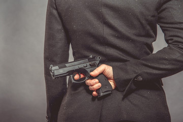pistol in hand hidden behind agent's back. portrait of woman with gun on grey background, copy space
