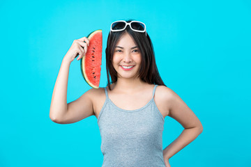 Attractive Asian young woman wearing summer vest and holding the Piece slide of watermelon on isolated blue color background, Sexy mouth bite, copy space and studio, fashion travel and tourist concept