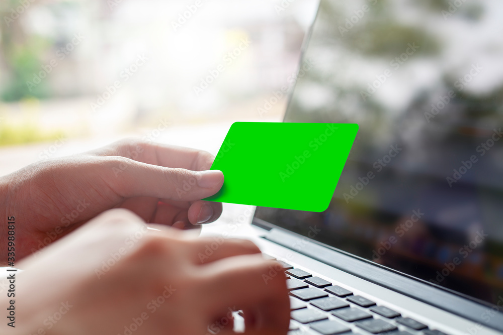 Wall mural hand holding blank green credit card and using modern laptop, typing and texting. against defocus gr