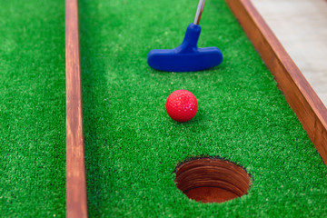 Mini golf. A golf club directs a red ball into the hole.