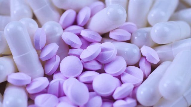 small purple pills and white capsules lie together on a table and rotate closeup