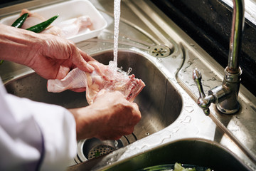Hands of man rinsing chicken thigh under tap water