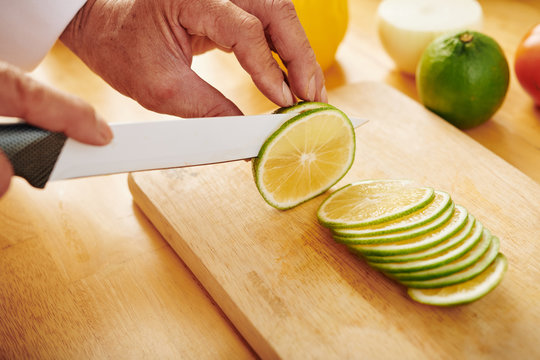 Close-up image of man slicing fresh ripe lime on wooden cutting board