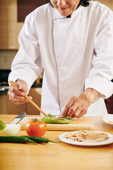 Smilling mature man in white chef coat wrapping boiled chicken meat in letture leaves to make healthy snacks