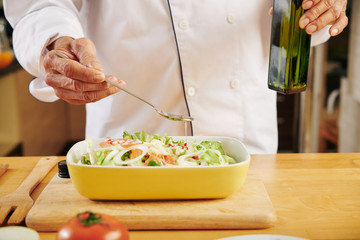 Chef pouring spoon of vegetable oil in bowl of fresh salad he made for lunch