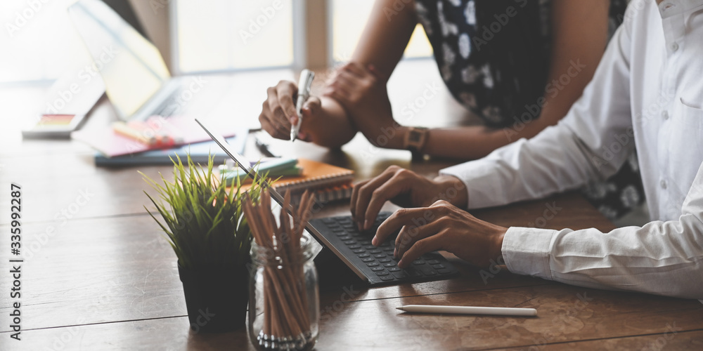 Poster cropped image of marketing team holding a stylus pen and typing on computer tablet with keyboard cas