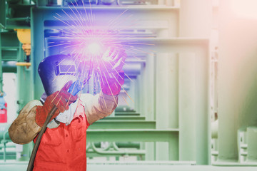 Worker welding position overhead steel pipe line in Oil refinery Industry worker at the factory steel structure with spark light weld by Mig weld holder close up and copy space.