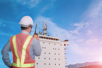 Worker with talkie in hand holding speaking radio in Shipyard The bulk carrier general cargo ship in dry dock yard, navigation bridge deck, recondition of hull repairing and repainting,  © TawanSaklay