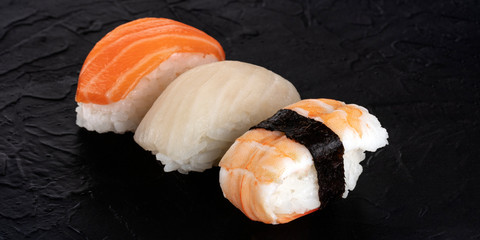 Nigiri sushi set panorama on a black background. Fresh salmon, white fish, and shrimp on rice
