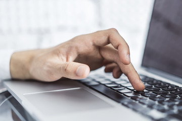 Male hands typing on laptop keyboard in sunny office, business and technology concept. Close up
