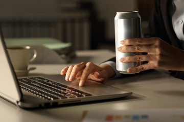 Executive hands with laptop holding energy drink can at night