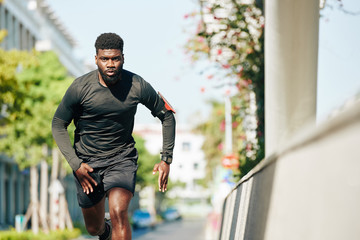 Serious concentrated Black young man running in the street when training for marathon