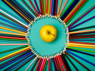 Colored pencils are laid out in a circle and apple on blue background