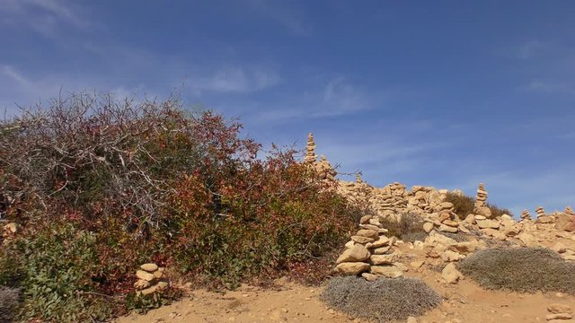 Pyramid of stones on top of a hill against the blue sky. Zoom out.
