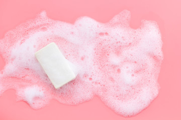 Soap bar with bubbles on pink background top-down