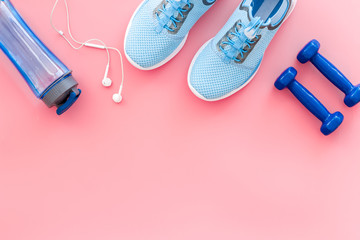 Sport background with sneakers and dumbbells on pink table top view copy space