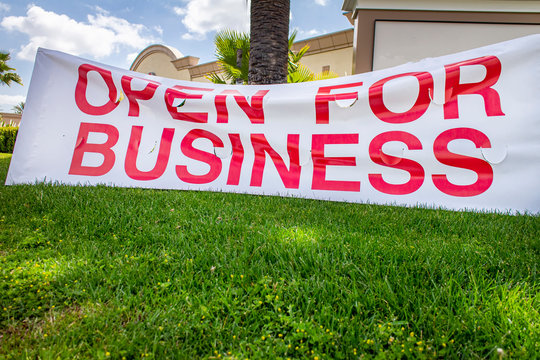 Open for Business Sign in white with red letters sagging in front of shopping center