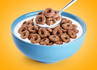 Bowl and spoon with chocolate corn rings, milk, yogurt on orange background.