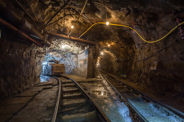 Fototapeta na wymiar Underground gold mine tunnel with rails two ways and light