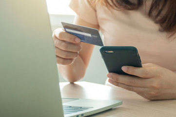 Female hands using smartphone and laptop computer for online shopping at home. Hand holding mobile phone with payment detail page display and credit card, Online shopping and stay home concepts.