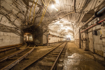 Naklejka na ściany i meble Underground gold mine tunnel with rails two ways and light