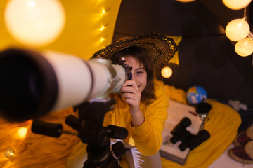 Small girl using telescope at home living room in a tent.